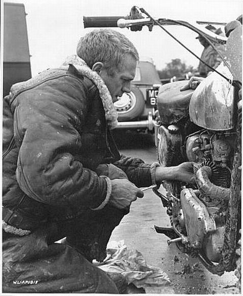 Steve McQueen works on his motorbike on the set. Candid.